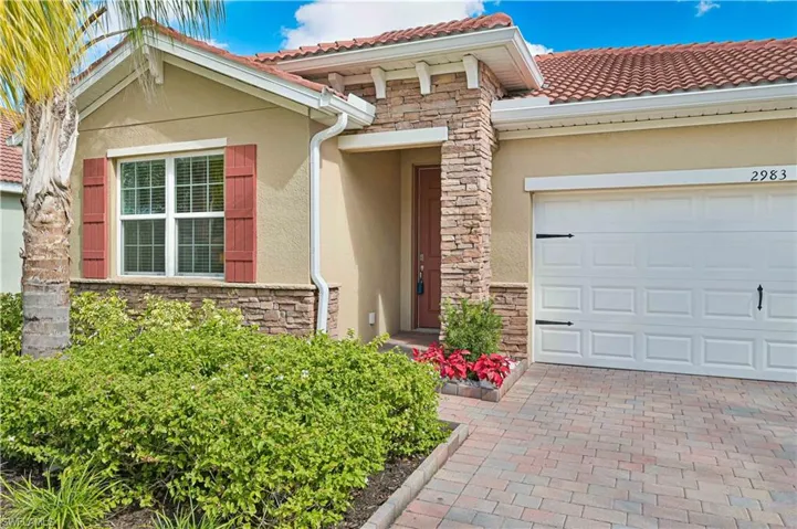 Doorway to property featuring stone siding, stucco siding, decorative driveway, and a tiled roof
