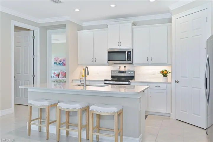 Kitchen featuring stainless steel appliances, white cabinets, backsplash, ornamental molding, and a breakfast bar area
