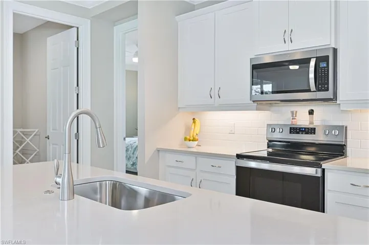 Kitchen with stainless steel appliances, white cabinetry, light stone counters, and crown molding