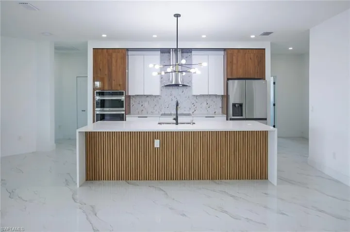 Kitchen featuring appliances with stainless steel finishes, sink, a center island with sink, white cabinetry, and hanging light fixtures