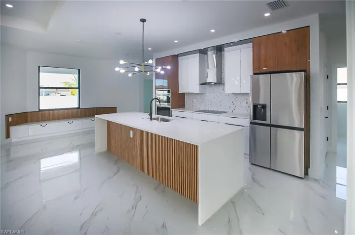 Kitchen featuring pendant lighting, a kitchen island with sink, white cabinets, wall chimney range hood, and stainless steel appliances