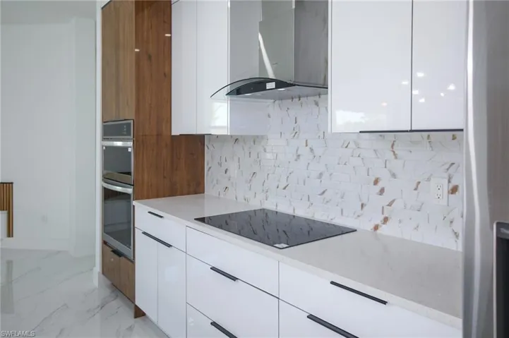 Kitchen with white cabinets, wall chimney exhaust hood, black electric cooktop, and tasteful backsplash