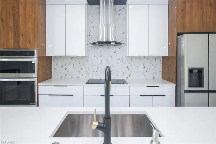 Kitchen with white cabinetry, sink, stainless steel appliances, wall chimney range hood, and tasteful backsplash