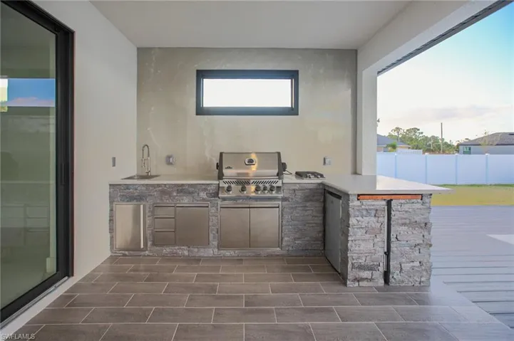 View of patio with area for grilling, a grill, and an outdoor wet bar