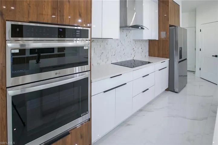 Kitchen with white cabinets, appliances with stainless steel finishes, backsplash, and wall chimney range hood