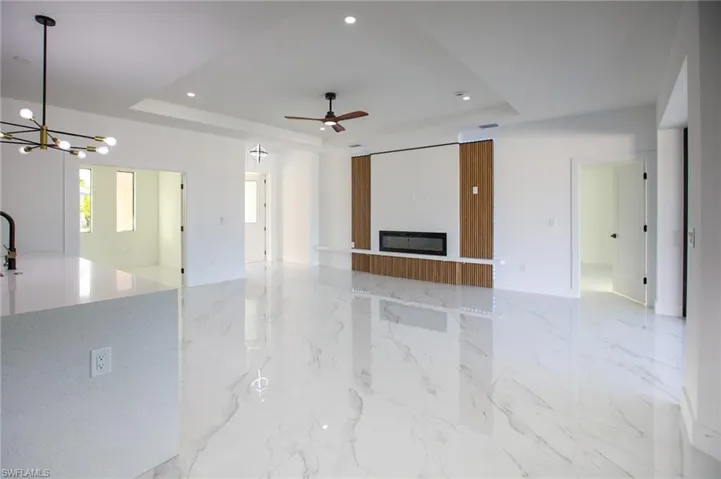 Unfurnished living room with ceiling fan with notable chandelier and a tray ceiling