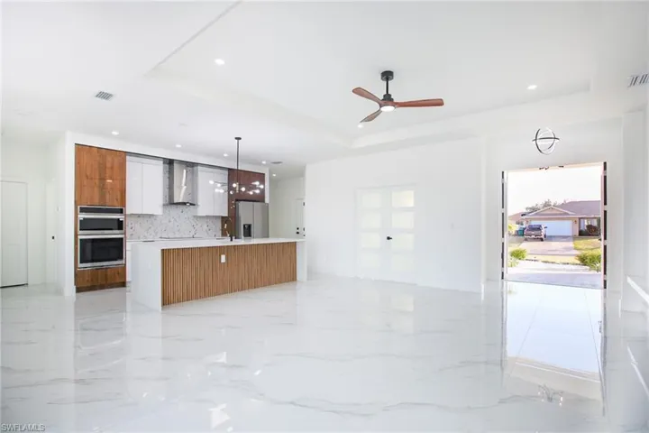 Kitchen with stainless steel appliances, a raised ceiling, wall chimney range hood, a large island with sink, and hanging light fixtures