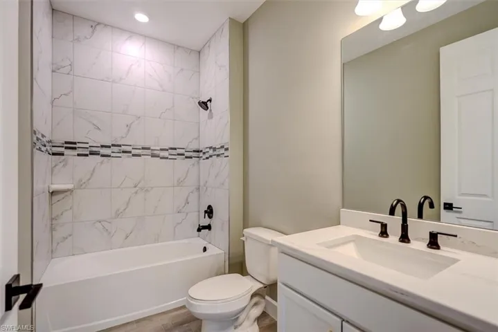 Full bathroom with wood-type flooring, tiled shower / bath, vanity, and toilet