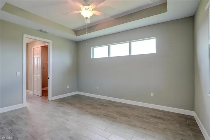 Empty room with ceiling fan, a raised ceiling, and light hardwood / wood-style floors