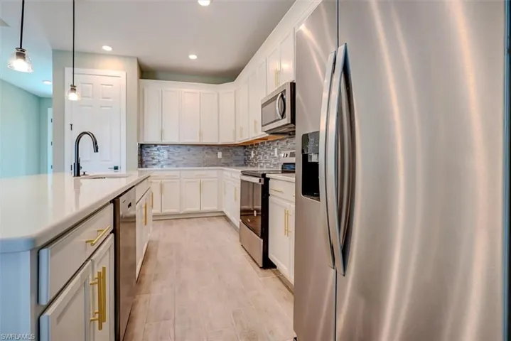 Kitchen featuring pendant lighting, an island with sink, sink, white cabinetry, and appliances with stainless steel finishes