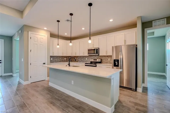 Kitchen featuring stainless steel appliances, white cabinetry, a center island with sink, and sink