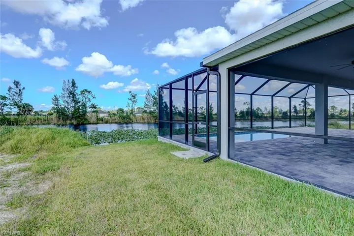 View of yard featuring a water view, glass enclosure, ceiling fan, and a patio area