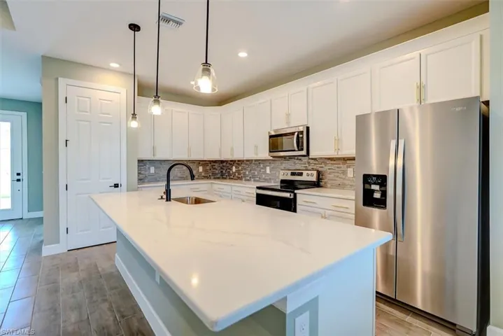 Kitchen with an island with sink, light stone counters, white cabinets, stainless steel appliances, and sink