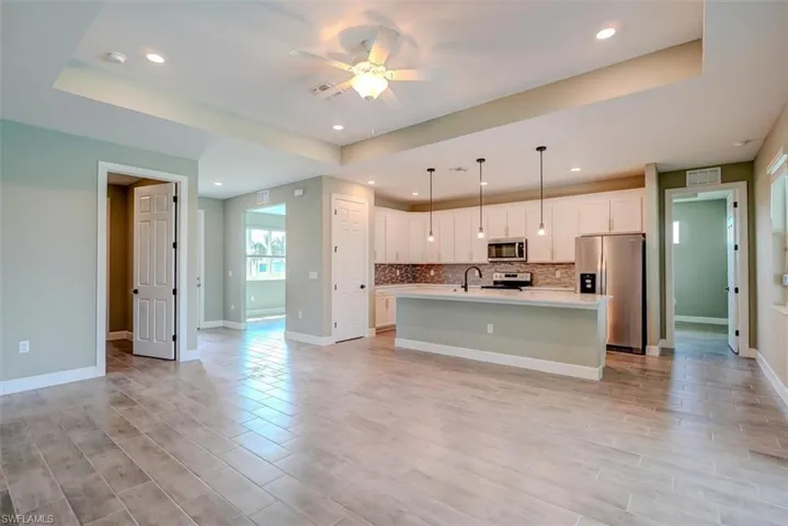 Kitchen with an island with sink, white cabinetry, ceiling fan, and stainless steel appliances