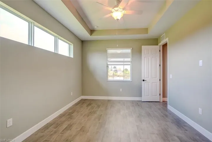Unfurnished room with light wood-type flooring, a tray ceiling, ceiling fan, and plenty of natural light