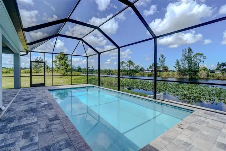 View of swimming pool with glass enclosure, a water view, and a patio