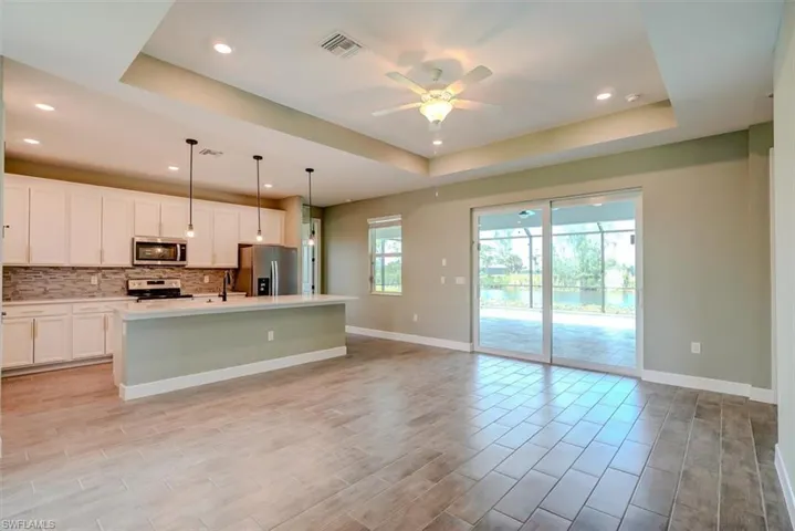 Kitchen featuring a raised ceiling, stainless steel appliances, light wood-type flooring, ceiling fan, and a center island with sink