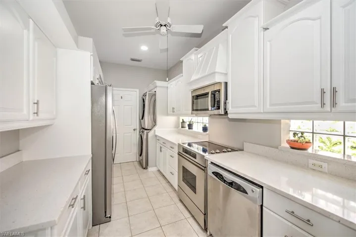 Kitchen featuring light stone countertops, appliances with stainless steel finishes, white cabinets, laundry area and light tile floors