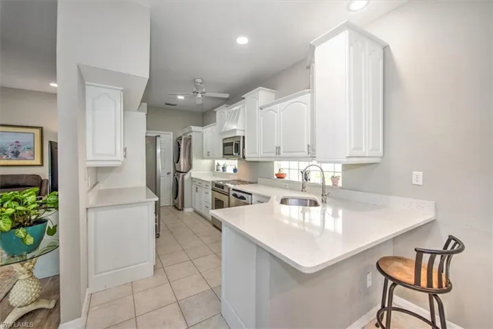 Kitchen featuring kitchen peninsula, white cabinetry, stainless steel appliances, sink, and laundry area