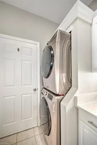 Laundry area for stacked washer and clothes dryer, cabinets, and light tile floors off kitchen area