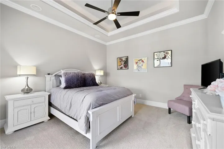 Bedroom with light carpet, a raised ceiling, ornamental molding, and a ceiling fan