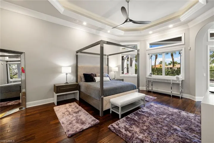 Bedroom with arched walkways, a raised ceiling, dark wood finished floors, ornamental molding, and a ceiling fan