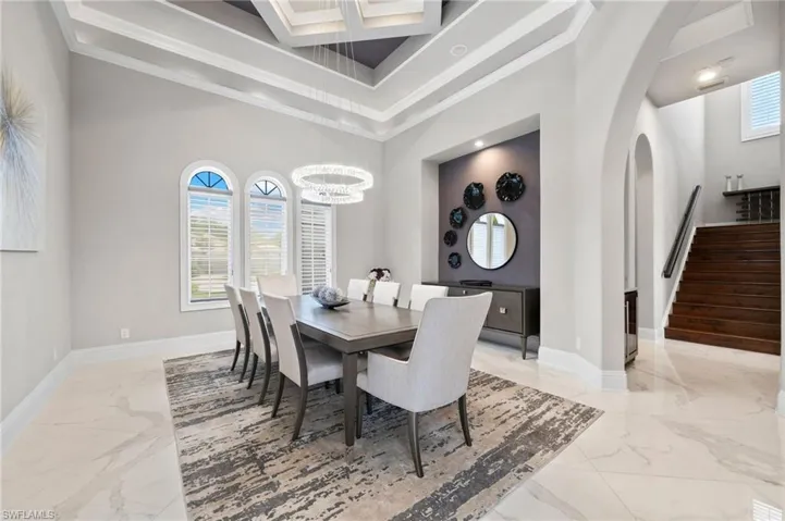 Dining area with light marble finish flooring, a towering ceiling, stairs, healthy amount of natural light, and a chandelier