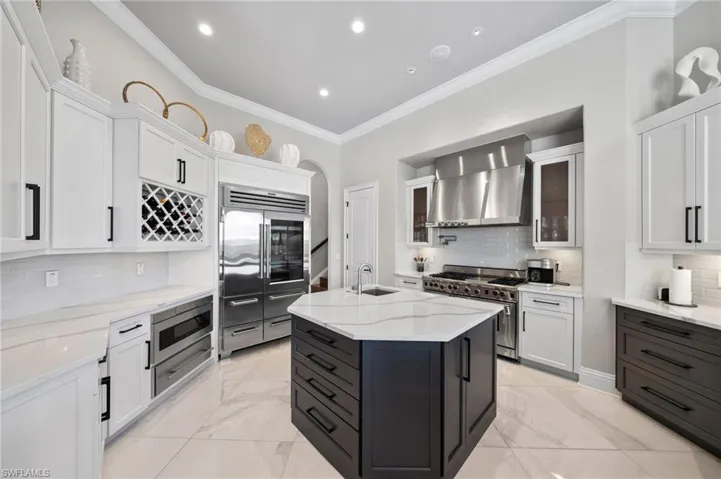 Kitchen with built in appliances, wall chimney exhaust hood, light marble finish floors, tasteful backsplash, and crown molding
