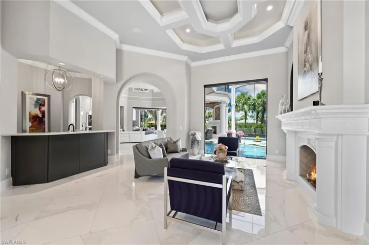 Living room featuring arched walkways, light marble finish flooring, plenty of natural light, crown molding, and a warm lit fireplace