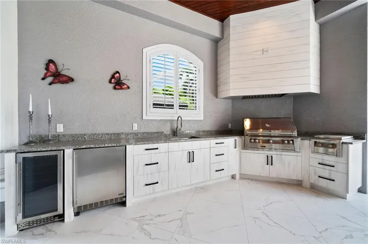 Kitchen featuring wine cooler, stainless steel fridge, light marble finish flooring, a textured wall, and dark stone counters
