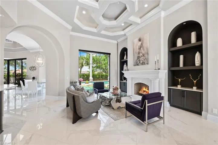 Living area with crown molding, built in shelves, light marble finish flooring, arched walkways, and a towering ceiling