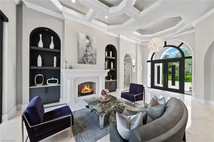 Living area featuring built in shelves, light marble finish floors, arched walkways, ornamental molding, and a chandelier