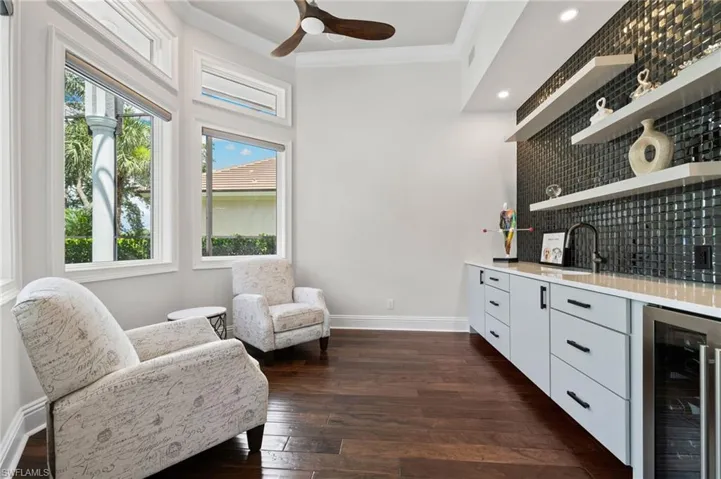 Sitting room featuring wine cooler, wet bar, dark wood-type flooring, a ceiling fan, and ornamental molding