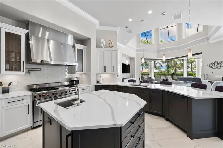 Kitchen featuring wall chimney exhaust hood, double oven range, light marble finish floors, a center island with sink, and ornamental molding