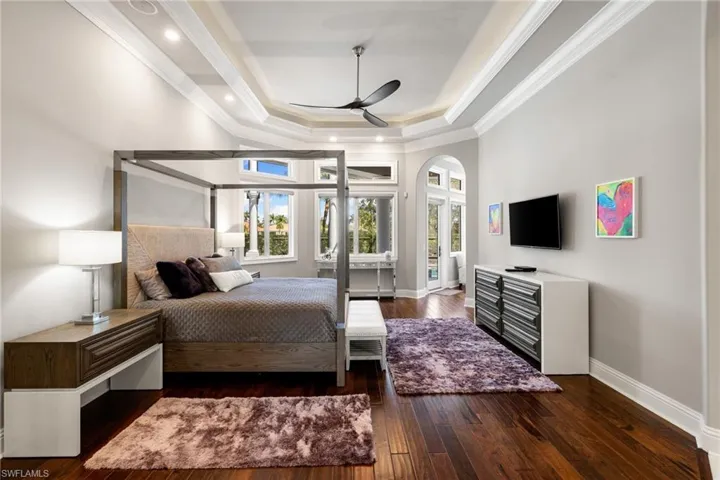 Bedroom with dark wood-style floors, crown molding, access to outside, arched walkways, and a tray ceiling