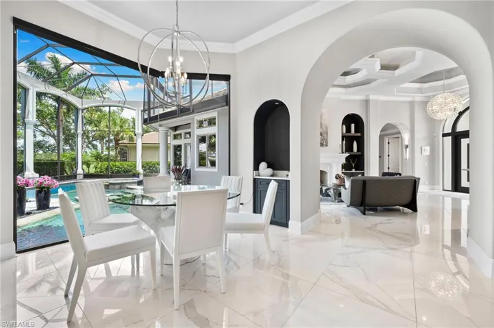 Dining room with ornamental molding, marble tiled floors, coffered ceiling, a chandelier, and arched walkways
