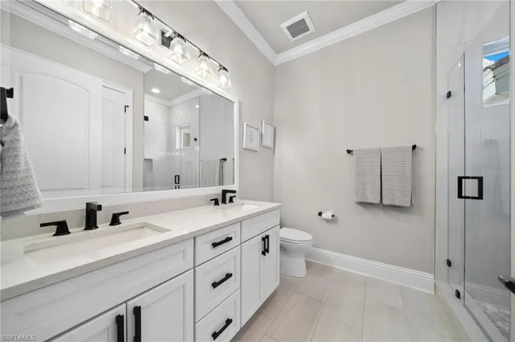 Bathroom featuring double vanity, crown molding, and a stall shower