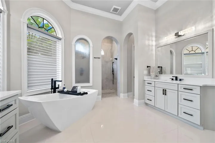 Full bath with a walk in shower, vanity, a freestanding bath, crown molding, and healthy amount of natural light