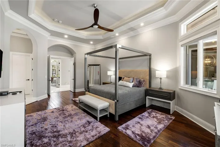 Bedroom with a raised ceiling, dark wood-type flooring, ornamental molding, a ceiling fan, and recessed lighting