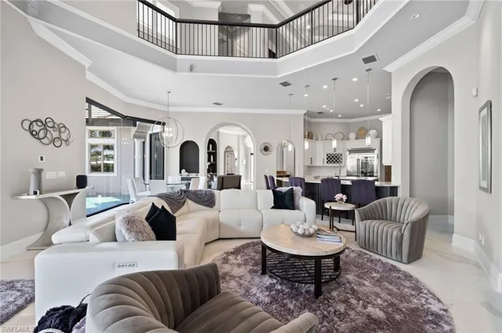 Living room featuring arched walkways, a towering ceiling, light marble finish floors, a chandelier, and ornamental molding