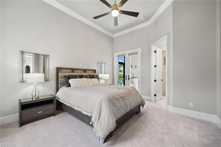 Bedroom featuring light colored carpet, ornamental molding, a towering ceiling, and a ceiling fan