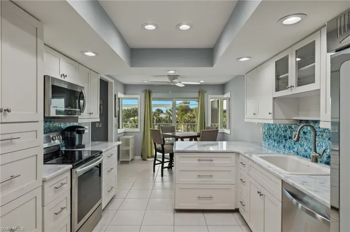 Kitchen featuring glass insert cabinets, tasteful backsplash, appliances with stainless steel finishes, light stone countertops, and recessed lighting
