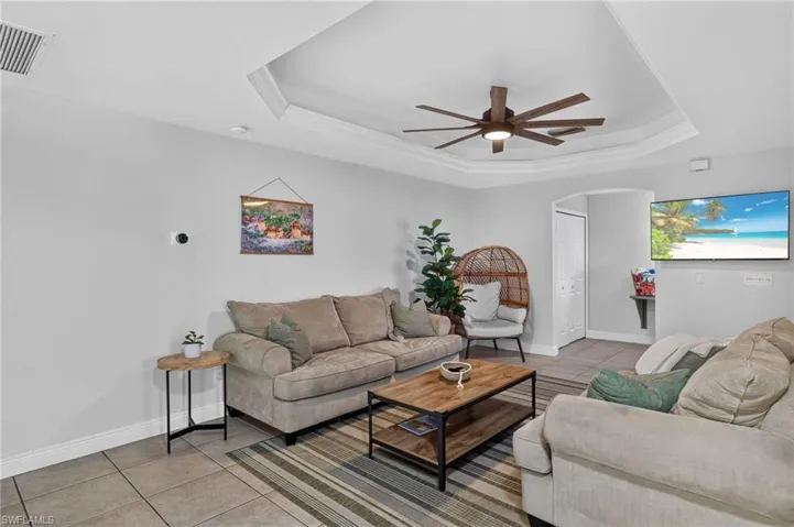 Tray ceiling with crown molding, ceiling fan with light fixture, gray tile flooring, light gray wall paint, and an arched doorway