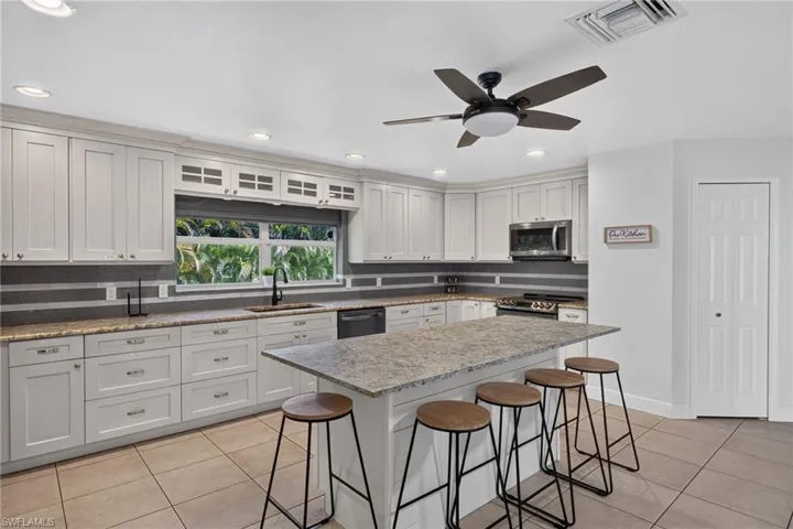 Spacious kitchen featuring an extended island with seating, white shaker-style cabinetry, granite countertops, and stainless steel appliances