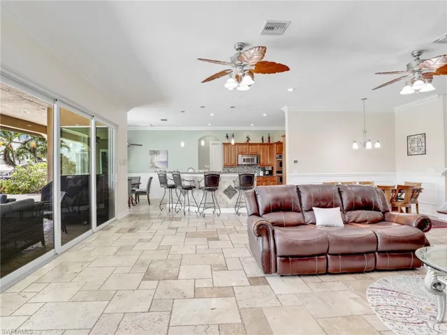 Living room with ornamental molding, light tile flooring, and ceiling fan with notable chandelier
