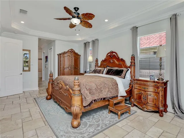 Bedroom featuring ceiling fan, a tray ceiling, ornamental molding, and light tile floors