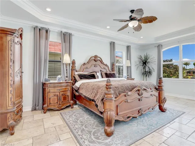 Tiled bedroom with ornamental molding, ceiling fan, and a tray ceiling