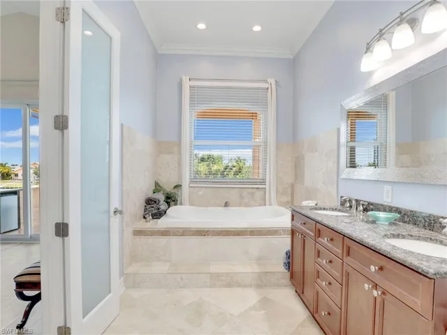 Bathroom featuring ornamental molding, tile floors, tile walls, dual vanity, and a relaxing tiled bath