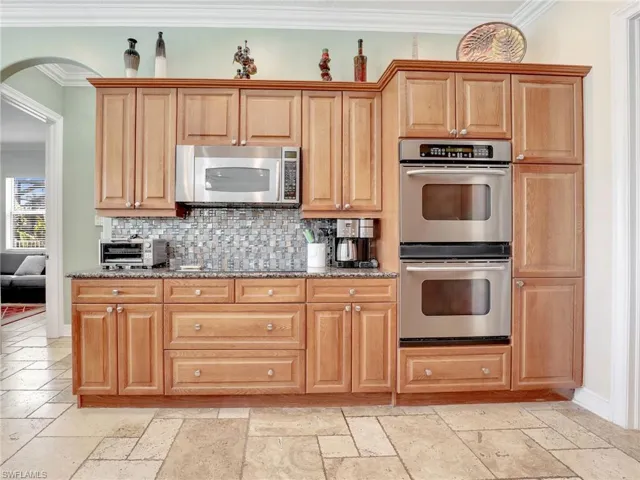 Kitchen with appliances with stainless steel finishes, light stone countertops, light tile floors, and crown molding