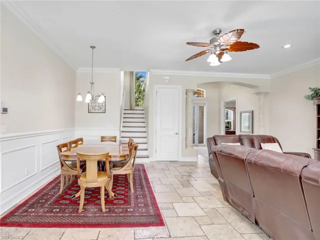 Dining space featuring decorative columns, light tile flooring, ceiling fan with notable chandelier, and crown molding